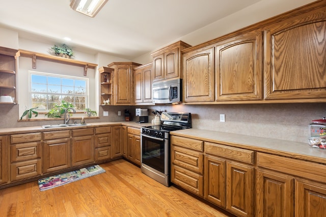 kitchen featuring brown cabinets, open shelves, appliances with stainless steel finishes, a sink, and light wood-type flooring