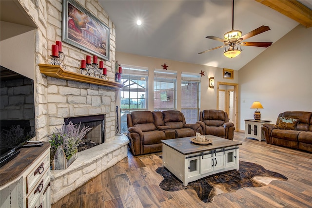 living room featuring lofted ceiling with beams, a ceiling fan, a stone fireplace, and wood finished floors