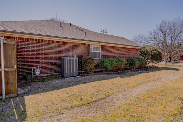 exterior space featuring a yard, brick siding, a shingled roof, and cooling unit