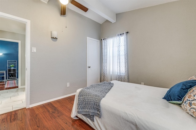 bedroom with a textured wall, lofted ceiling with beams, a ceiling fan, wood finished floors, and baseboards