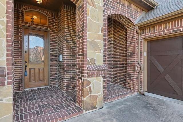 property entrance with a garage, a shingled roof, and brick siding