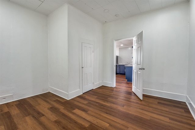 empty room featuring ornamental molding, dark wood finished floors, and baseboards