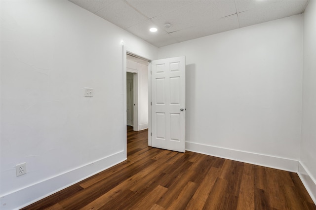 spare room featuring dark wood-style floors, a paneled ceiling, and baseboards