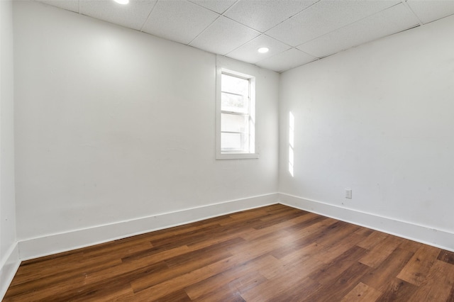 unfurnished room featuring dark wood-type flooring, a drop ceiling, and baseboards