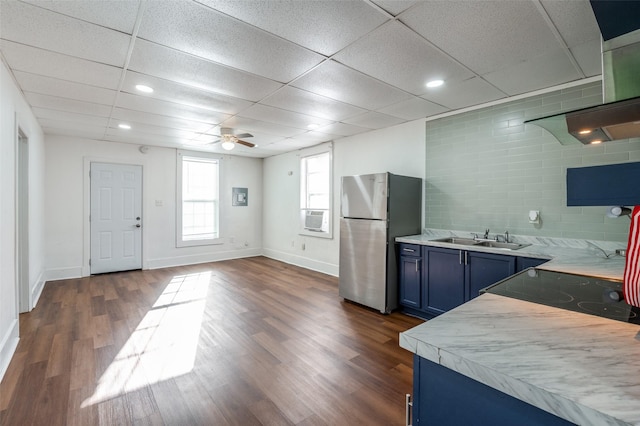 kitchen with a sink, light countertops, blue cabinetry, freestanding refrigerator, and wall chimney exhaust hood