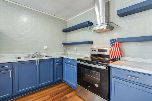 kitchen with stainless steel electric range oven, blue cabinetry, wall chimney range hood, open shelves, and a sink