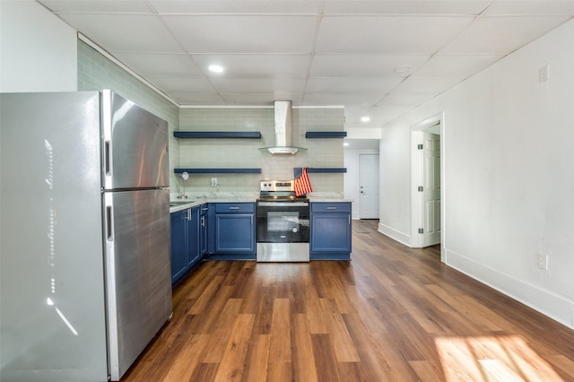 kitchen with blue cabinets, stainless steel appliances, wall chimney range hood, decorative backsplash, and open shelves