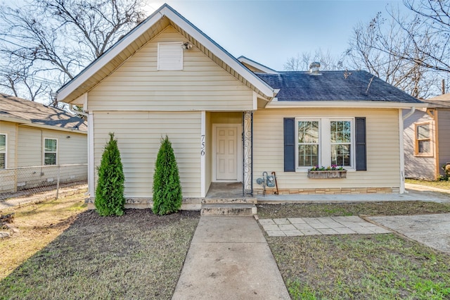 bungalow-style home with a shingled roof and fence