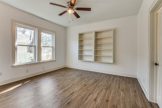 empty room with wood finished floors, a ceiling fan, and baseboards