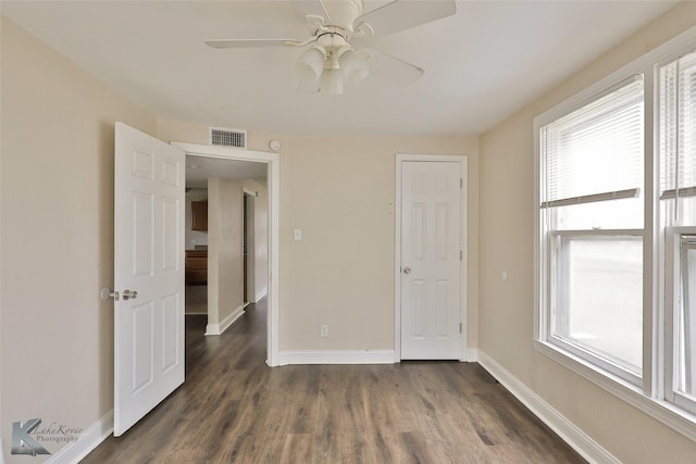 unfurnished bedroom featuring dark wood-type flooring, multiple windows, visible vents, and baseboards