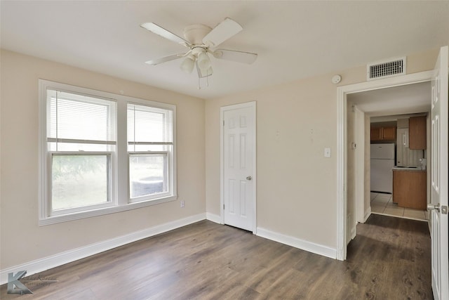 unfurnished bedroom featuring visible vents, a ceiling fan, baseboards, freestanding refrigerator, and dark wood finished floors