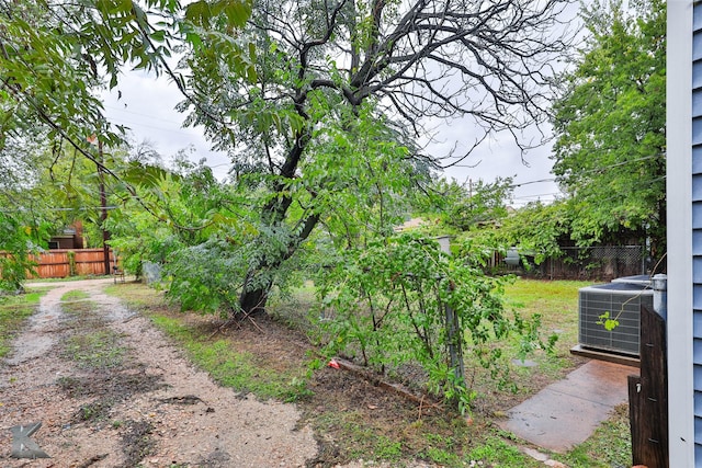 view of yard featuring fence, dirt driveway, and central AC unit