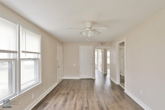 unfurnished room with a ceiling fan, wood finished floors, visible vents, and baseboards