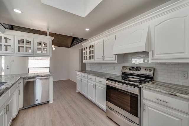 kitchen featuring stainless steel appliances, white cabinets, custom exhaust hood, light wood finished floors, and glass insert cabinets