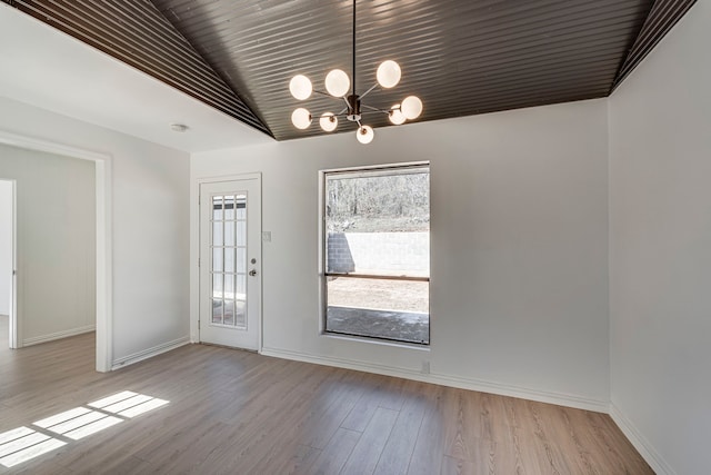 unfurnished dining area featuring a chandelier, vaulted ceiling, baseboards, and wood finished floors