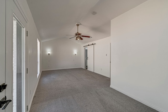 empty room featuring a barn door, baseboards, a ceiling fan, vaulted ceiling, and carpet floors