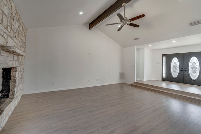 unfurnished living room featuring visible vents, beamed ceiling, wood finished floors, a stone fireplace, and french doors