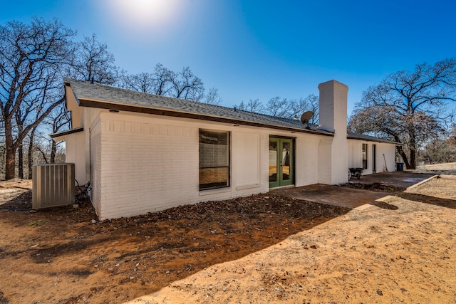 back of property with french doors, brick siding, a patio, a chimney, and cooling unit