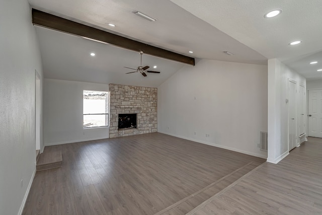 unfurnished living room with vaulted ceiling with beams, a stone fireplace, wood finished floors, a ceiling fan, and baseboards