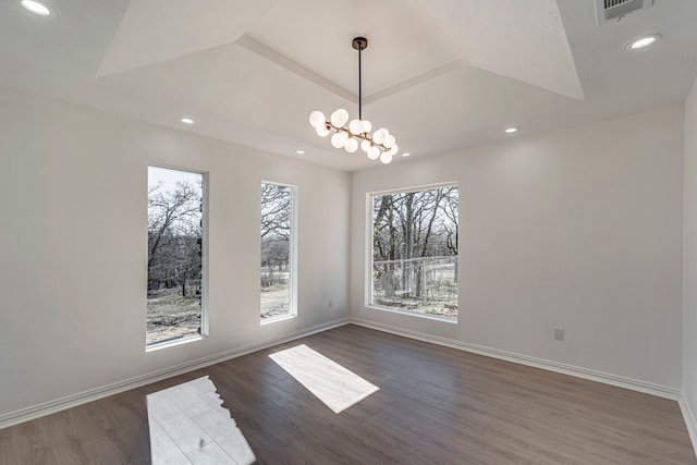 unfurnished dining area with dark wood-style floors, a tray ceiling, a notable chandelier, recessed lighting, and baseboards