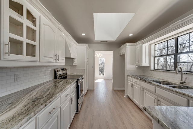 kitchen with stainless steel range with electric stovetop, white cabinets, a sink, and light stone countertops