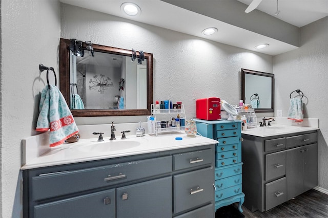 bathroom with a textured wall, wood finished floors, two vanities, and a sink