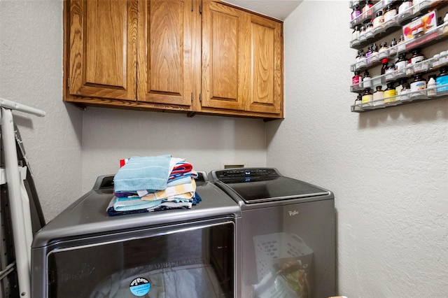 clothes washing area with washer and dryer, cabinet space, and a textured wall