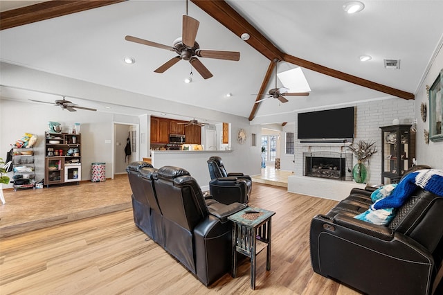 living area with a fireplace, light wood finished floors, visible vents, lofted ceiling with beams, and a ceiling fan