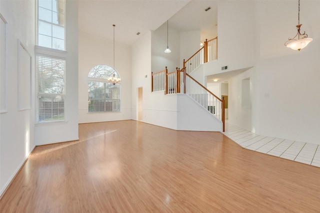 unfurnished living room with a chandelier, stairway, wood finished floors, and a towering ceiling