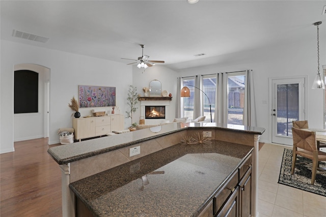 kitchen featuring arched walkways, open floor plan, a glass covered fireplace, and visible vents