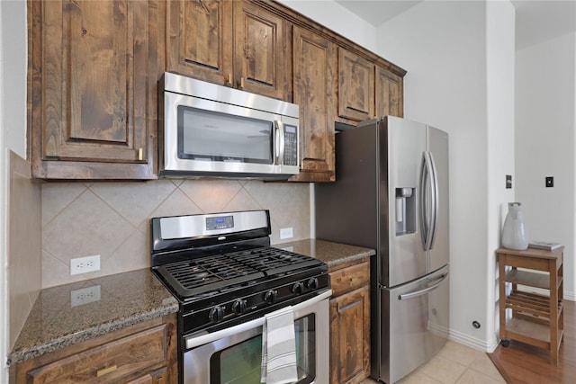 kitchen with appliances with stainless steel finishes, backsplash, dark stone countertops, and light tile patterned floors