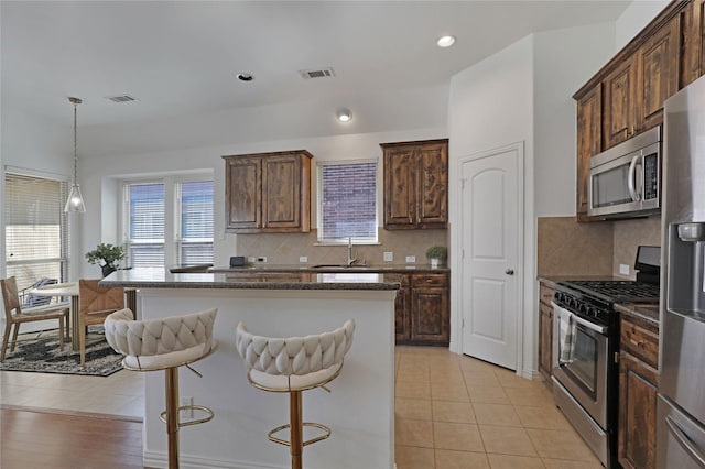 kitchen with light tile patterned floors, stainless steel appliances, a breakfast bar, a kitchen island, and a sink