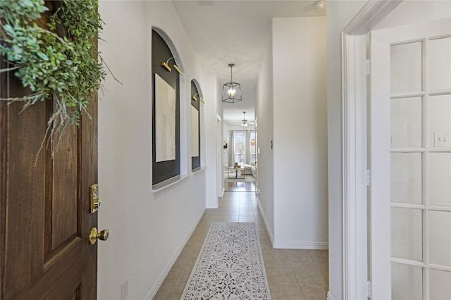 hall featuring baseboards, arched walkways, and light tile patterned flooring