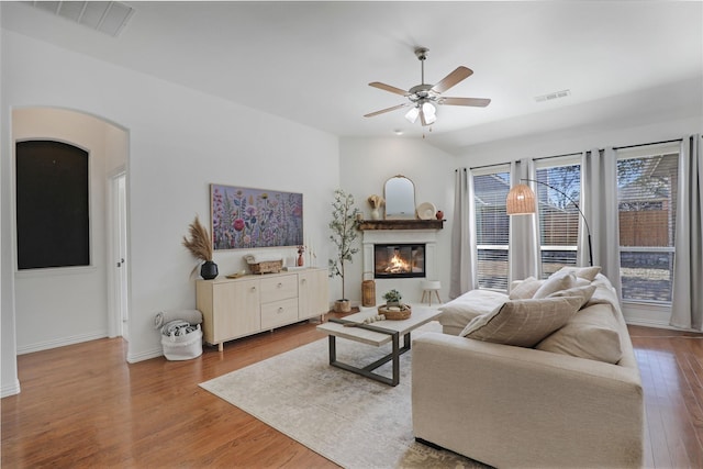 living area featuring a glass covered fireplace, visible vents, arched walkways, and wood finished floors