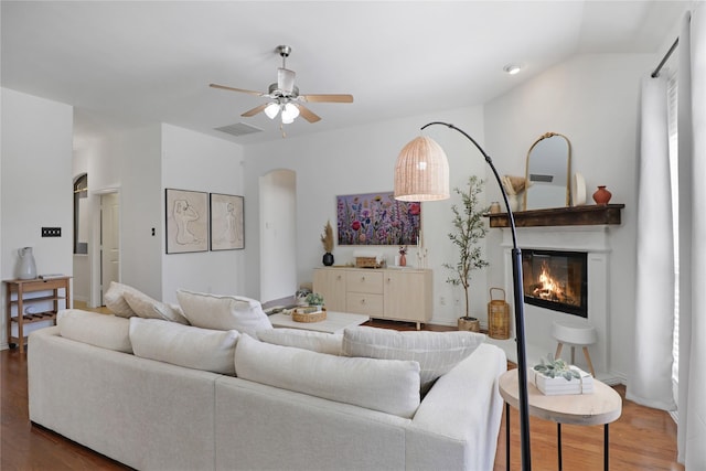 living area featuring arched walkways, a glass covered fireplace, wood finished floors, and visible vents