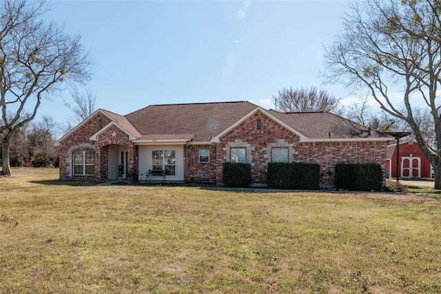 ranch-style home with a front yard, brick siding, an outbuilding, and roof with shingles