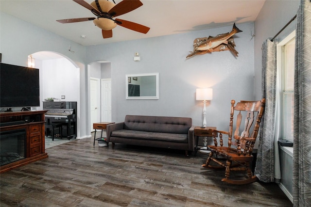 living room featuring arched walkways, a fireplace, ceiling fan, and wood finished floors