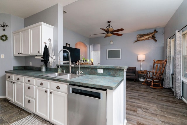 kitchen with white cabinets, dark countertops, a peninsula, stainless steel dishwasher, and a sink