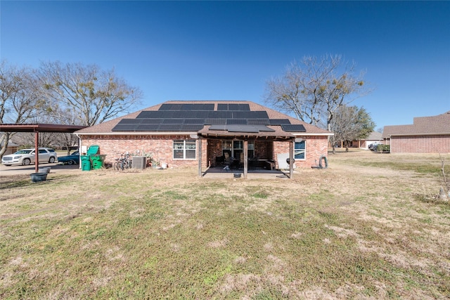 back of property with a patio area, a yard, brick siding, and solar panels