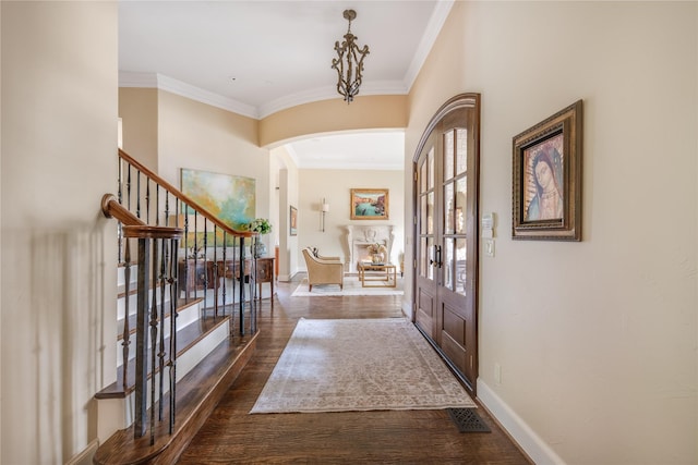 entrance foyer with dark wood-style floors, baseboards, ornamental molding, and arched walkways