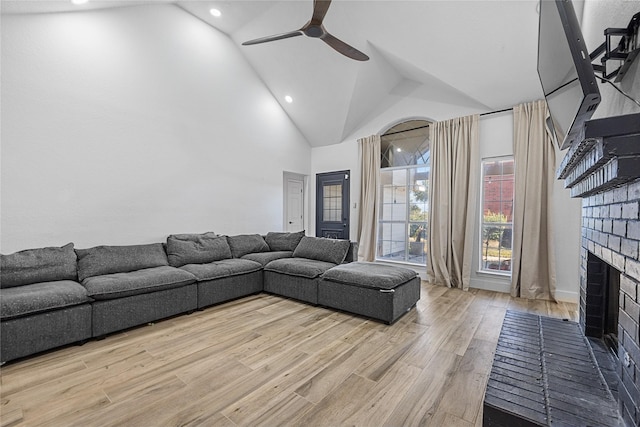 living area featuring ceiling fan, light wood-style floors, a fireplace, high vaulted ceiling, and recessed lighting