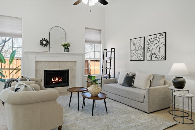 living area with a ceiling fan, plenty of natural light, a tiled fireplace, and tile patterned floors