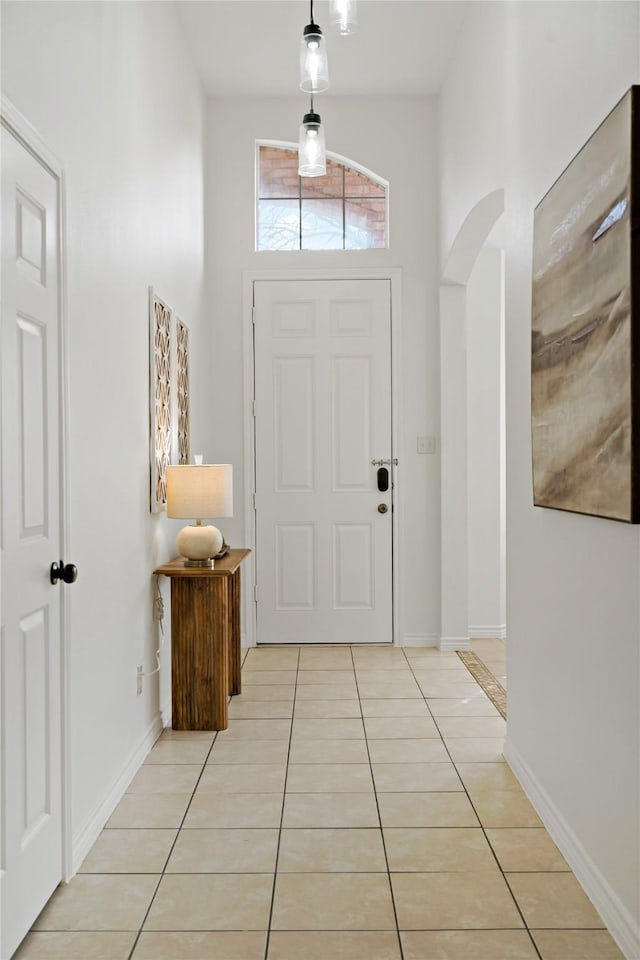 foyer with a towering ceiling, light tile patterned floors, baseboards, and arched walkways