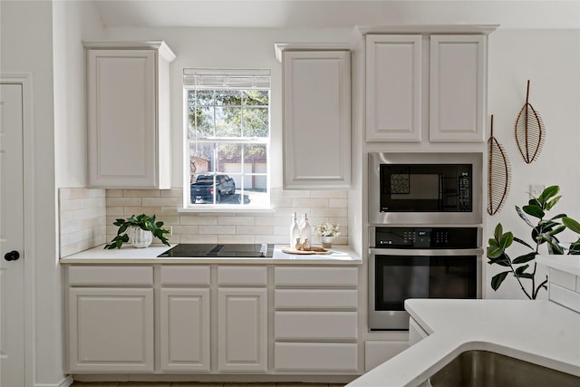 kitchen with tasteful backsplash, oven, black electric stovetop, built in microwave, and white cabinetry