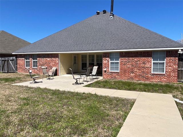 back of house with a yard, brick siding, a shingled roof, and a patio area