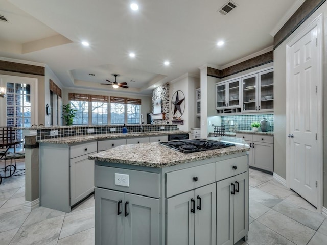 kitchen featuring visible vents, a center island, a tray ceiling, black electric cooktop, and a sink