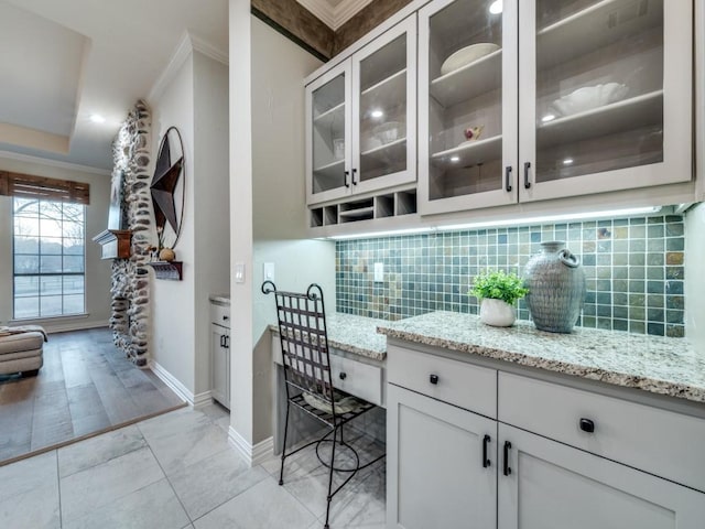 interior space featuring light stone countertops, tasteful backsplash, glass insert cabinets, and crown molding