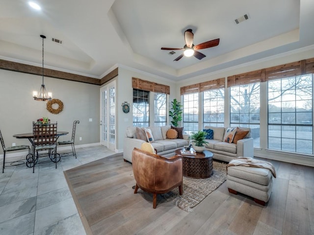 living room featuring ceiling fan with notable chandelier, light wood-style flooring, a raised ceiling, and visible vents