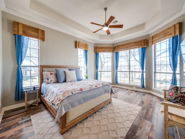 bedroom with visible vents, baseboards, a raised ceiling, and wood finished floors