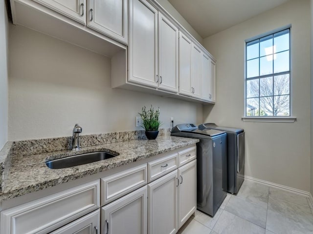 clothes washing area featuring cabinet space, baseboards, a sink, and washing machine and clothes dryer